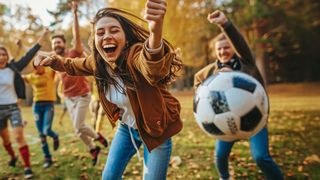 Herbstmeisterschaften Gruppe junger Menschen rennt jubelnd durch einen herbstlichen Park und ein Ball fliegt vorbei