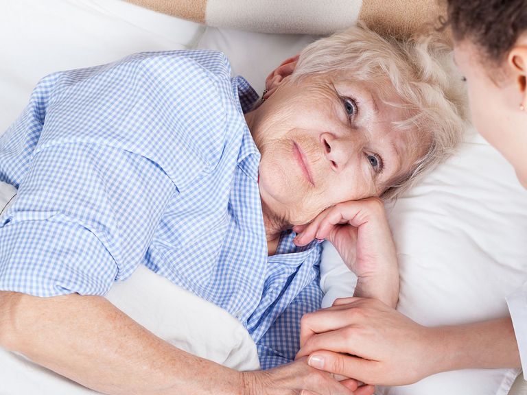 Ältere Frau im Bett wird von junger Pflegerin versorgt