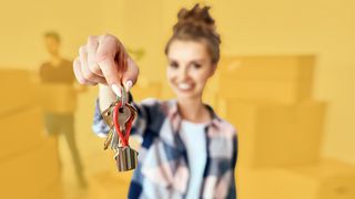 Junge Frau mit Umzugskartons zeigt neuen Schlüssel