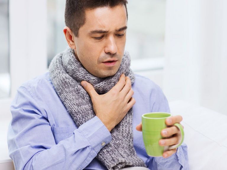 Mann mit Schal ist heiser und trinkt heißen Tee