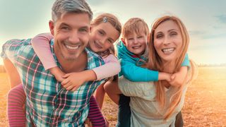 IKK-Gesundheitskonto Eltern mit ihren zwei Kindern huckepack lachen in die Kamera