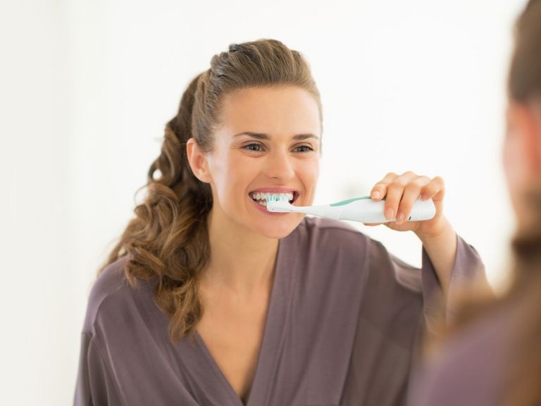 Schwangere Frau putzt vor einem Spiegel die Zähne