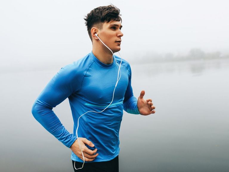 Junger Sportler mit blauem Oberteil joggt bei Tagesausklang