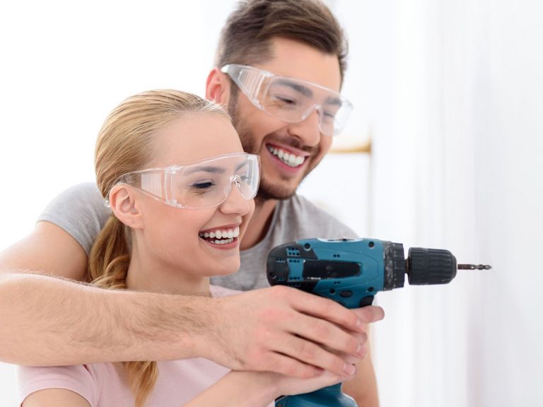 Mann hilft seiner Frau beim Arbeiten mit einer Bohrmaschine