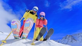 Mutter und Tochter in kompletter farbenfroher Skiausrüstung stehen lachend im Schnee