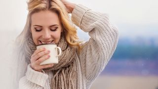 Junge Frau mit dickem Pullover und einer Tasse in der Hand