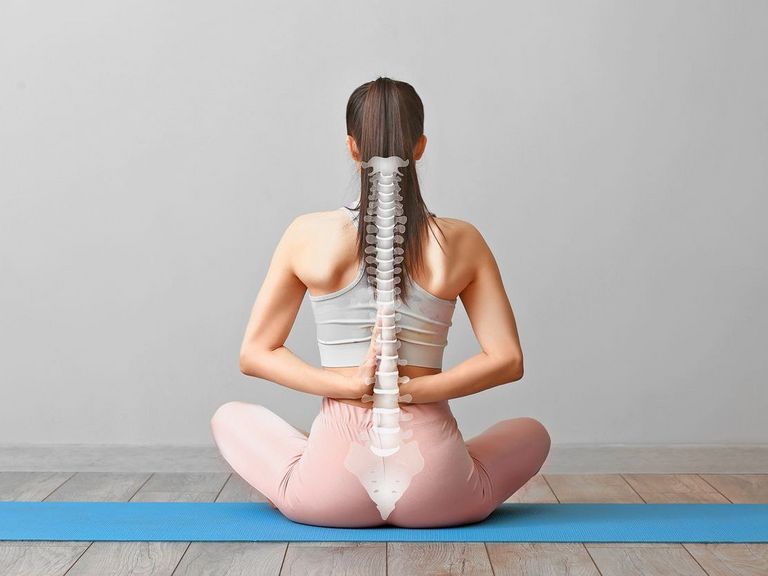 Frau in Sportkleidung sitzt auf eine Yogamatte und zeigt ihre Wirbelsäule