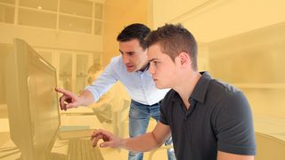 Junger Mann lässt sich am PC-Bildschirm etwas erklären