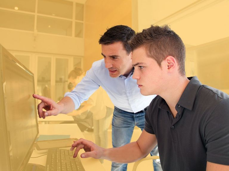 Junger Mann lässt sich am PC-Bildschirm etwas erklären