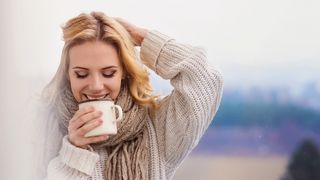 Junge Frau mit dickem Pullover und einer Tasse in der Hand