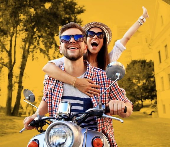 Zwei huttragende und jubelnde Studenten auf einem Roller