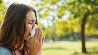 Allergiesaison Frau steht in einem Park und niest in ein Taschentuch