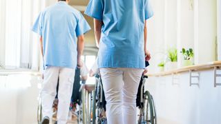 Vollstationäre Pflege Zwei Stationspfleger schieben Rollstühle mit Pflegebedürftigen