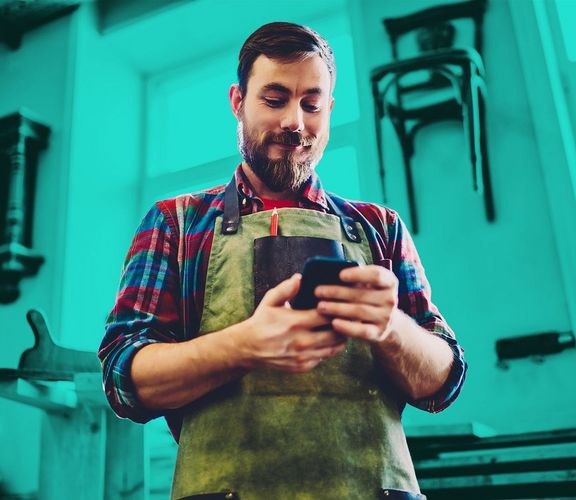 Digitalpaket Handwerker in seiner Werkstatt schaut auf sein Smartphone