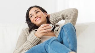 Frau mit einer Tasse Tee sitzt bequem auf dem Sofa