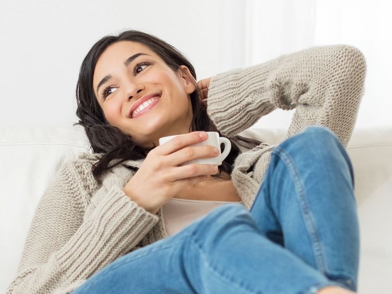 Frau mit einer Tasse Tee sitzt bequem auf dem Sofa