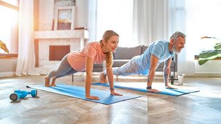 Mann und Frau sind in einer Liegestützposition auf Yogamatten in einem Wohnzimmer