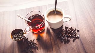 Ein Glas Tee und eine Tasse Kaffee stehen auf einem Holztisch