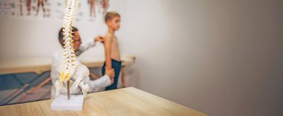 Junge während einer Untersuchung beim Orthopäden und im Bildvordergrund ist ein Wirbelsäulenskelett zusehen