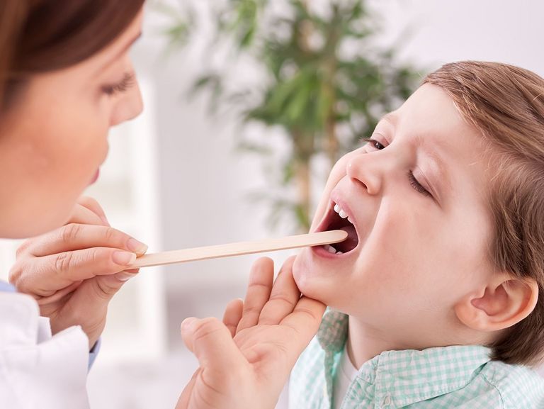 Ärztin schaut die Zunge eines kranken Jungen an