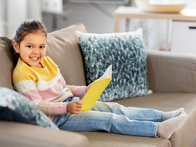 Mädchen sitzt auf einer Couch und hat ein Buch in der Hand
