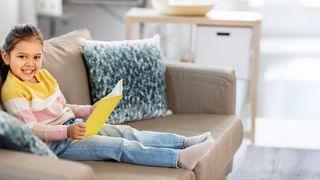 Geschichten zur Gesundheit Mädchen sitzt auf einer Couch und hat ein Buch in der Hand
