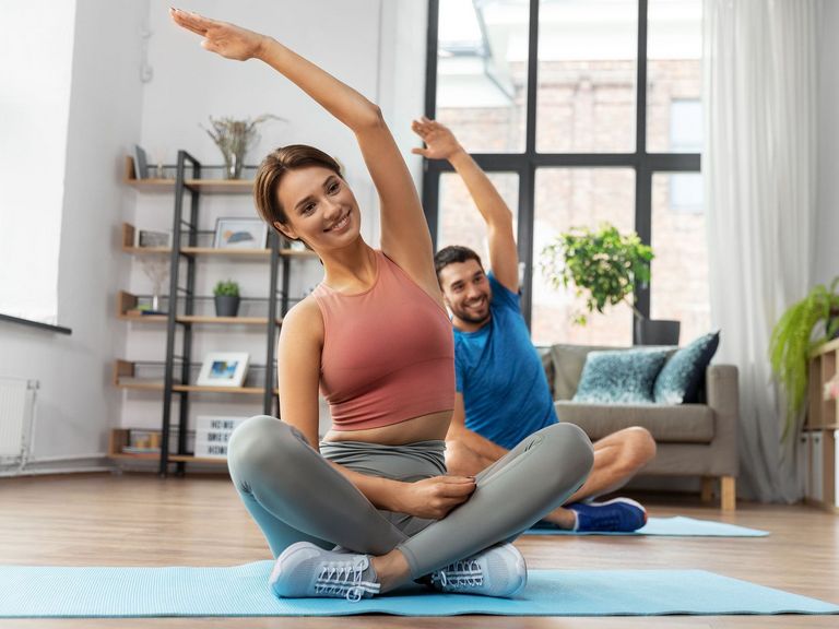 Pärchen im Schneidersitz auf Yogamatten macht Dehnübungen