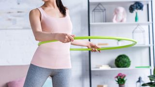 Sportlich gekleidete Frau nutzt in ihrem Wohnzimmer einen Hula-Hoop-Reifen