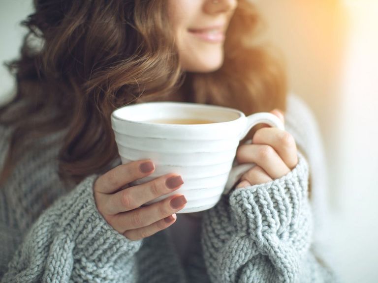 Frau in dickem Pullover und einer Tasse mit einem Heißgetränk in der Hand