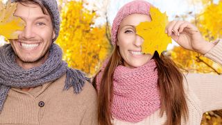 Lachendes Pärchen hält sich je ein Herbstblatt vor ein Auge