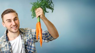 Karotten & Sehkraft Junger Mann hält ein Bund Karotten in die Höhe und lacht