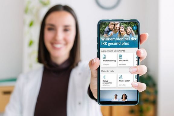 IKK Kunden-App Frau zeigt mit einem Lächeln das Display ihres Smartphones