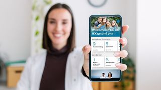 IKK Kunden-App Frau zeigt mit einem Lächeln das Display ihres Smartphones