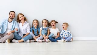 Gesunde Kindheit Sechsköpfige Familie sitzt nach Größe geordnet vor einer grauen Wand auf dem Boden