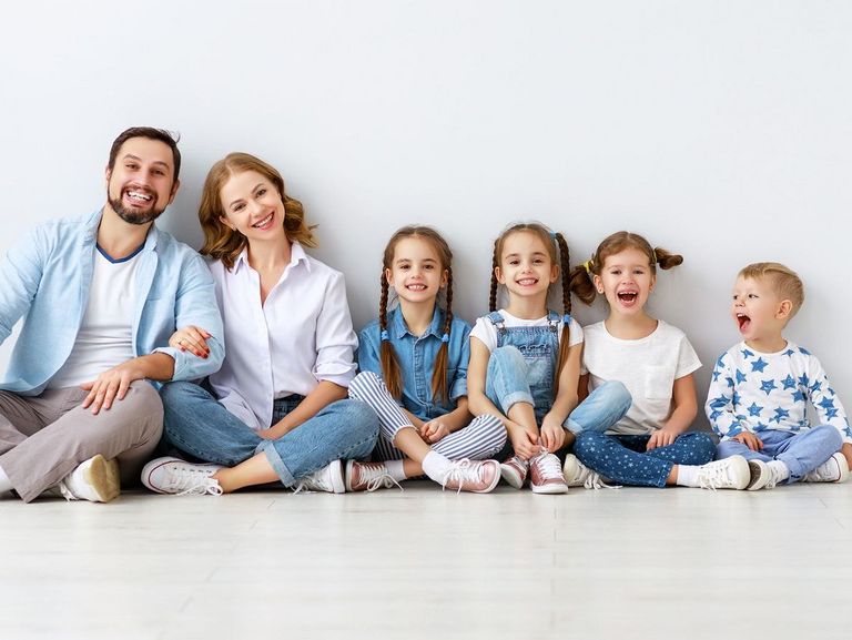 Sechsköpfige Familie sitzt nach Größe geordnet vor einer grauen Wand auf dem Boden