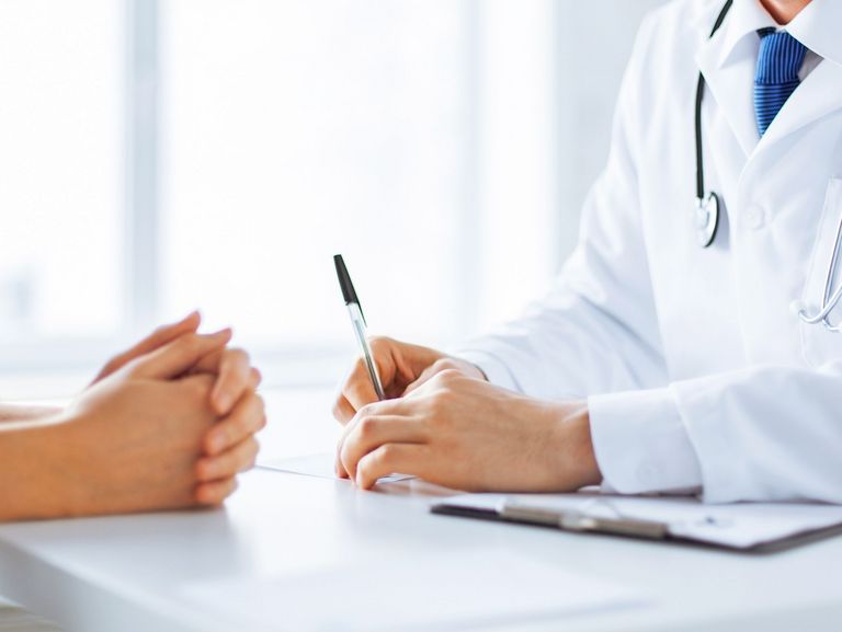 Patientin und Arzt mit Stethoskop sitzen an einem Schreibtisch und man sieht nur dir Hände