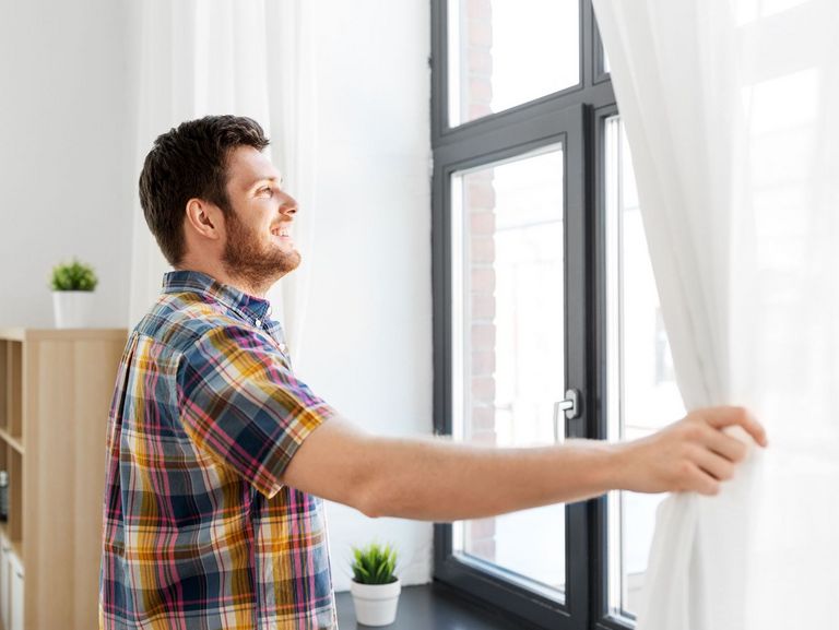 Mann möchte ein Fenster öffnen und schiebt dafür die Gardine beiseite