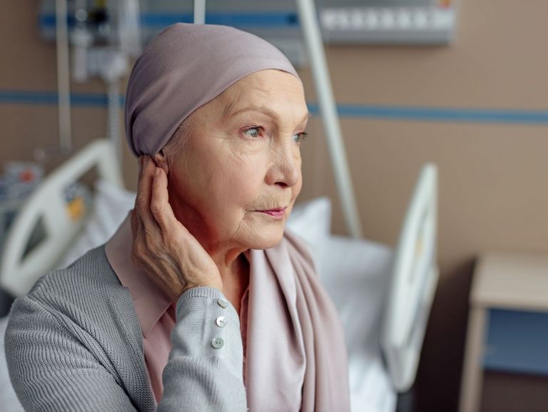Krebskranke ältere Frau sitzt gedankenverloren in einem Krankenhauszimmer