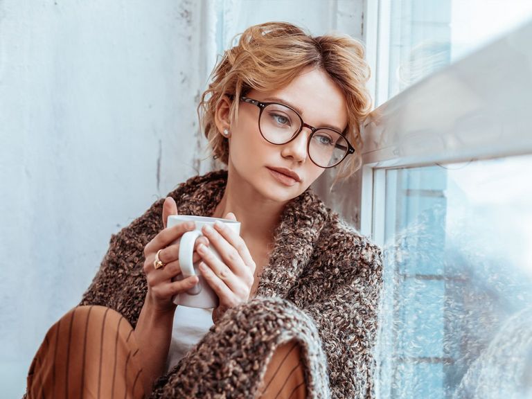 Frau sitzt traurig mit einer Tasse Tee einsam am Fenster