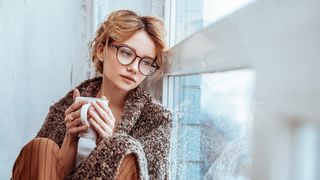 Frau sitzt traurig mit einer Tasse Tee einsam am Fenster