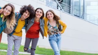 Azubi-Gesundheitstag im Handwerk Gruppe Jugendlicher in farbefrohen Klamotten schauen Schulter an Schulter und leicht nach vorn gebeugt gemeinsam lachend in die Kamera