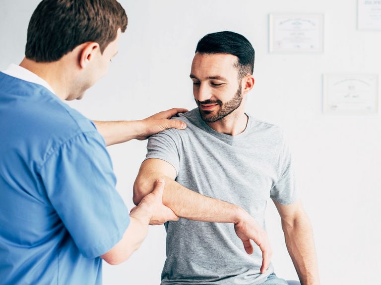 Mann sitzt beim Therapeuten, der seine Gelenke am Arm untersucht