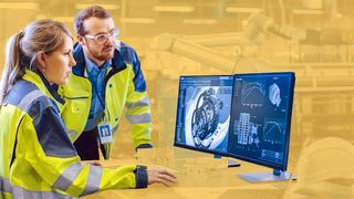 Frau und Mann arbeiten am PC-Bildschirmen in Fabrikhalle