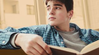 Jugendlicher sitzt verträumt auf einer Couch und hält ein Buch in den Händen