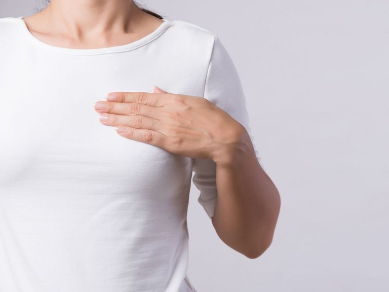 Frau in einem hellen T-Shirt hält ihre Hand oberhalb der Brust