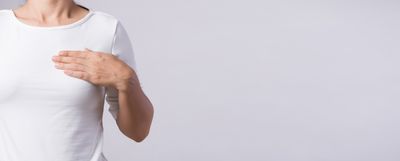 Frau in einem hellen T-Shirt hält ihre Hand oberhalb der Brust