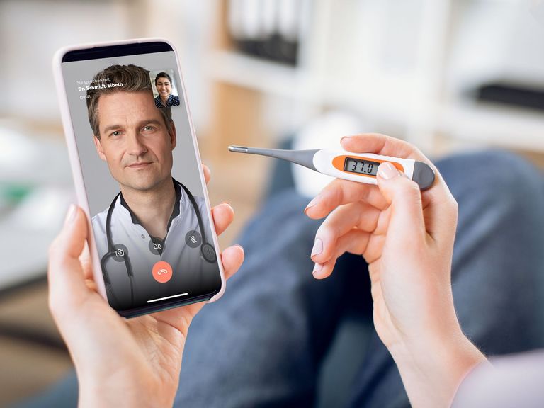Hände halten ein Fieberthermometer und ein Smartphone