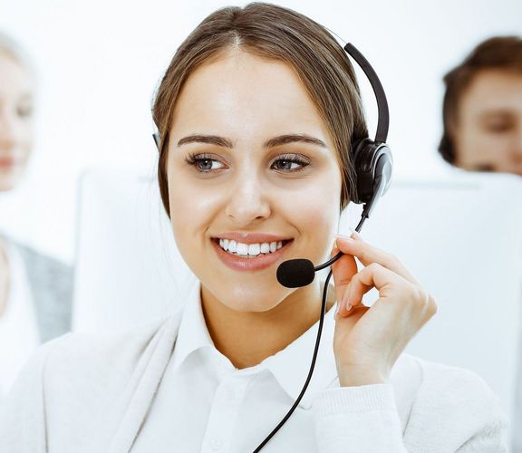 Junge Mitarbeiterin mit einem Headset führt gerade ein Telefongespräch