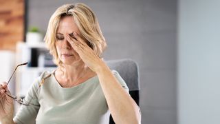 Office-Eye-Syndrom Frau sitzt im Büro vor einem Bildschirm und reibt sich erschöpft die Augen