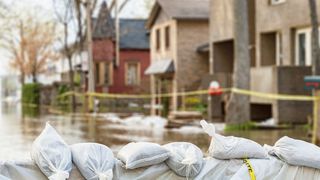 Hochwasser vor einer Häuserfront mit einer Barriere aus Sandsäcken im Bildvordergrund